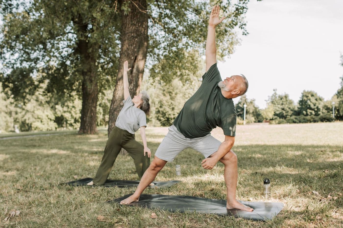 Older man and woman practicing yoga outdoors in a park